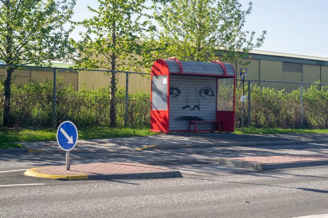 Röd och grå busskur med ansiktsgraffiti vid en väg, med träd i bakgrunden.